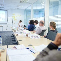 Project management instructor teaching a classroom in front of a slideshow. - Thumbnail